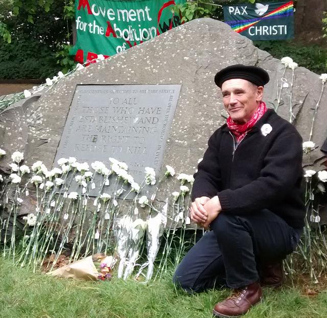 Man in front of a big stone with a plaque on it and white carnations