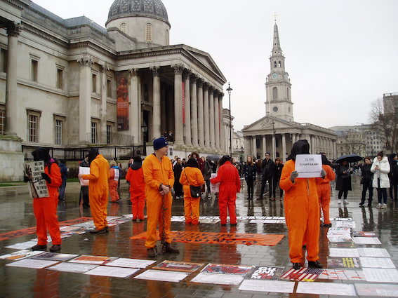 nine people in orange jump suits protesting about Guantanamo Bay outside the National Gallery in London