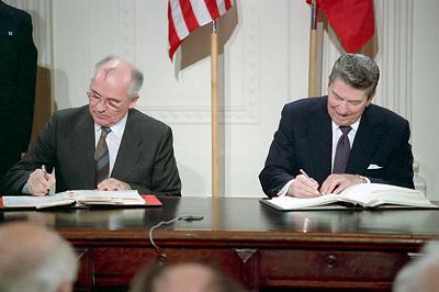 Gorbachev and Reagan sitting at a big desk signing documents