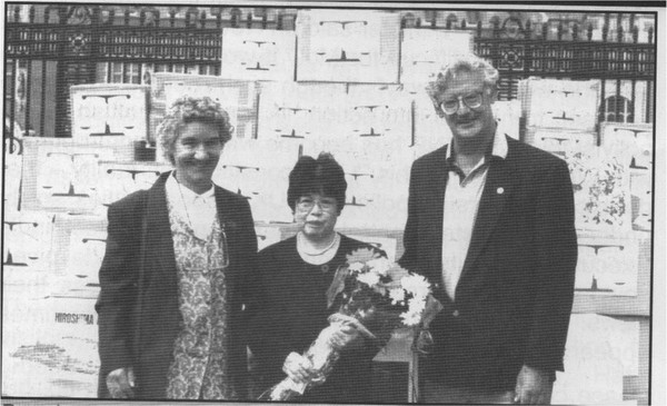 black and white photo of three people, the woman in the middle holds a bunch of flowers