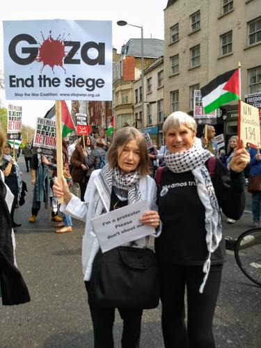 two protestors with a banners reading 'Gaza End the siege' and 'I'm a protestor please don't shoot me'