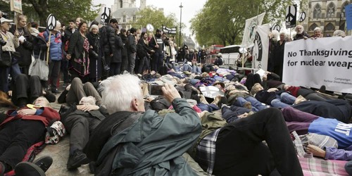 protestors lying down on the pavement, with CND signs and a banner reading 'No Thanksgiving for Nuclear Weapons'