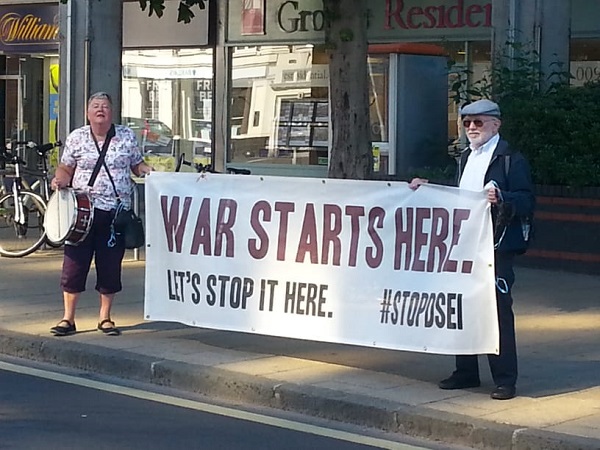Two people holding a banner reading WAR STARTS HERE – LET'S STOP IT HERE - hashtag stop DSEI