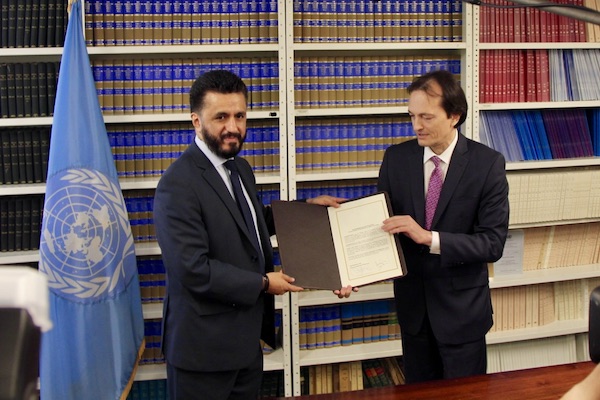 two men stand next to a United Nations flag holding a document