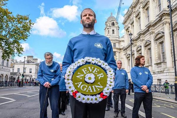 forces veterans in blue sweaters with a wreath of white poppies with two red poppies and inscribed 'never again'