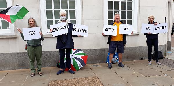 Four protestors with a Palestinian flag and placards reading 'Stop annexation in Palestine, Sanctions now, End apartheid'