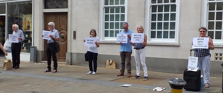 six people holding up signs saying '75 years ago today', 'UN nuclear ban', 'Britain should join' etc