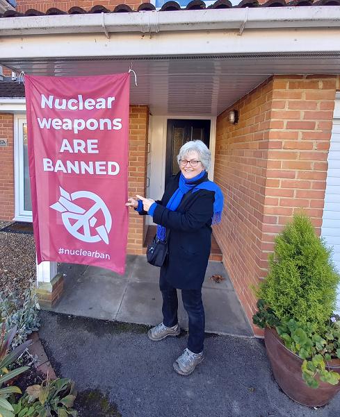 Banner: Nuclear weapons are banned, #nuclearban. Hilary in a scarf outside the front door of her house