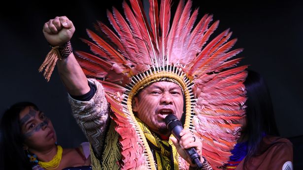 a man in a head-dress with red feathers making a speech